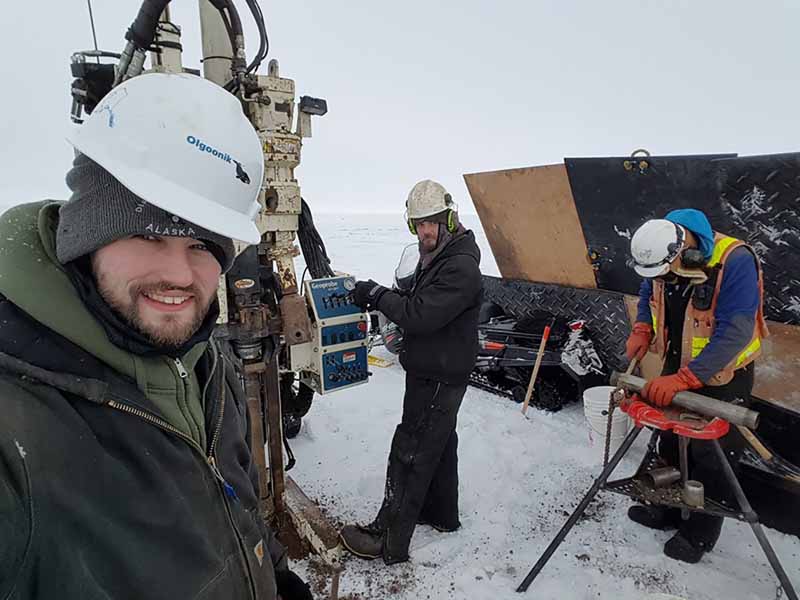 (l to r) Drillers Scott Bombard, Derek Dell and Project Engineer, Ryan Campbell, try to stay warm in their makeshift wind fort on the harsh tundra in northern Alaska.